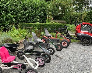 Gezellige buitenruimte bij Vakantiehuis in Riemst Millen, Limburg, Belgi met trapauto's voor kinderen omgeven door groene natuur.